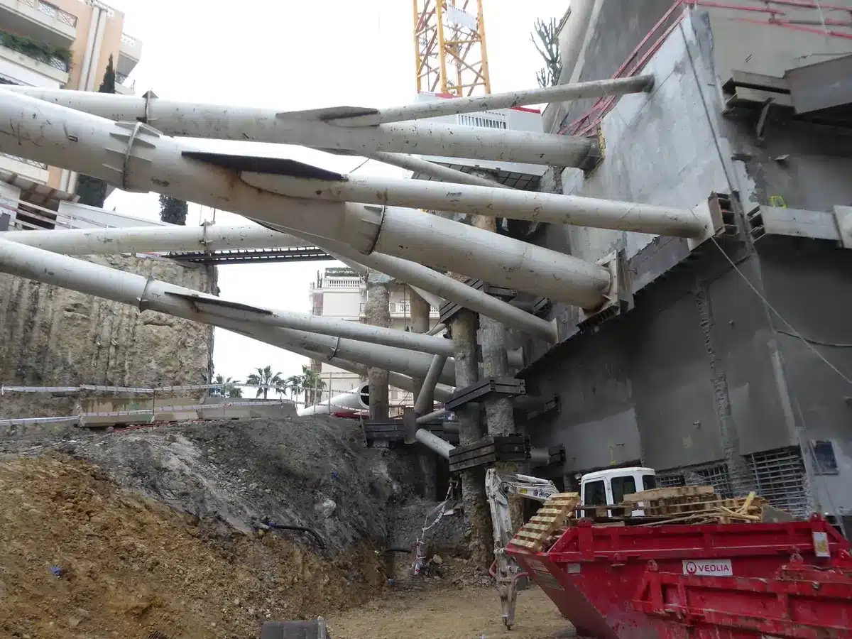 Soutènement par étais blancs sur un chantier d'excavation profonde avec grue et benne rouge Veolia.