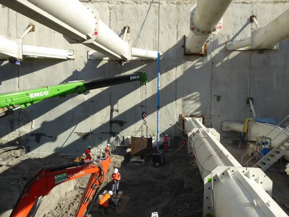 Chantier d'excavation avec grue Enco, pelleteuse Kubota et butons de soutènement blancs pour parois moulées.